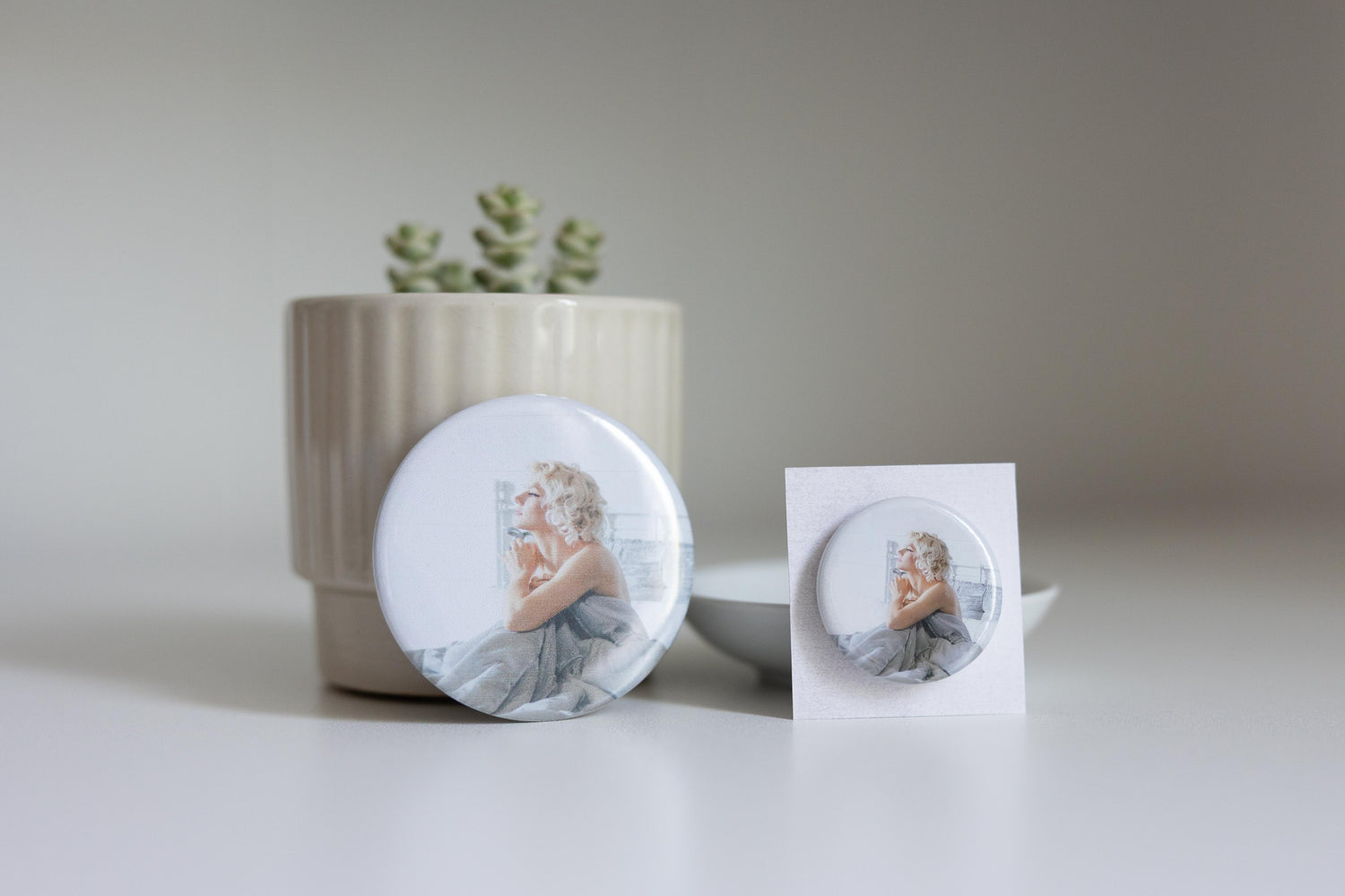 Custom round pin featuring a portrait, placed on a white surface with a plant in the background.
